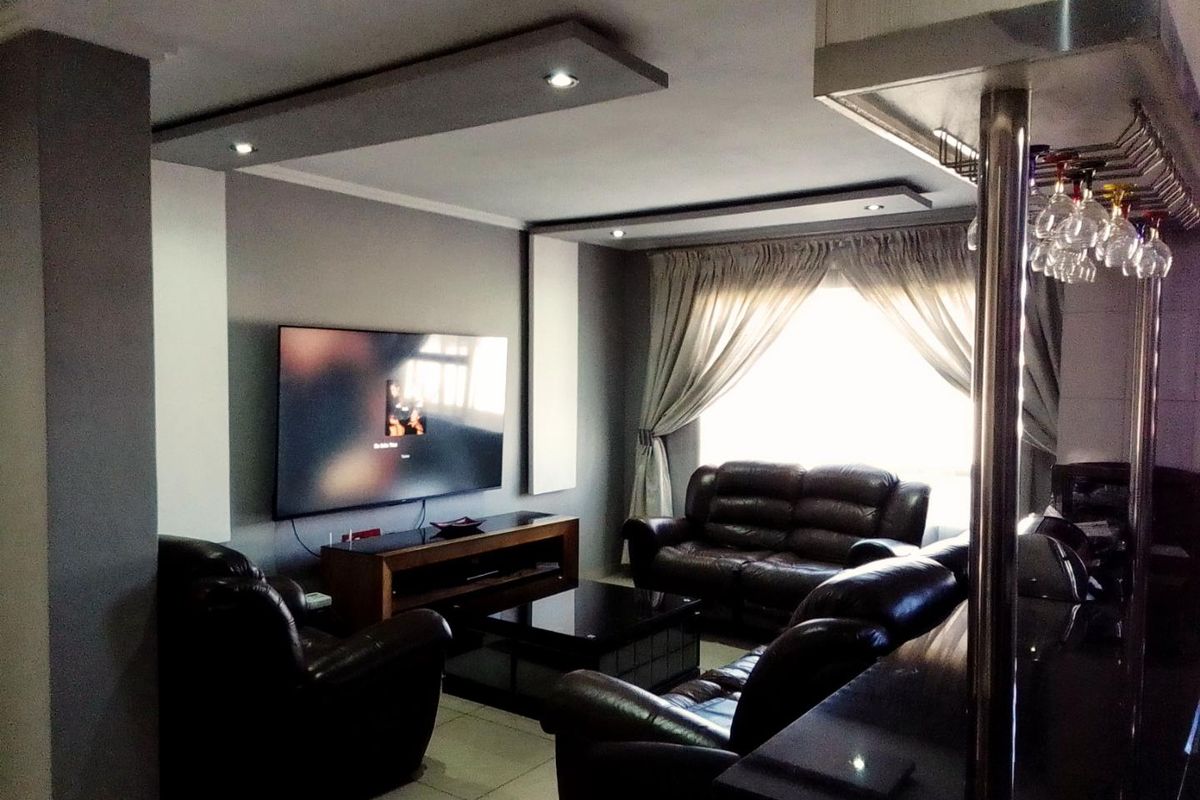 A comfortable living room featuring a dropped ceiling with recessed lighting, tiled floors, and an adjacent built-in bar area.