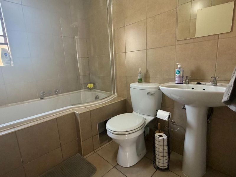 A functional bathroom featuring a bathtub with a glass screen, pedestal basin, and toilet, finished with neutral wall and floor tiling.