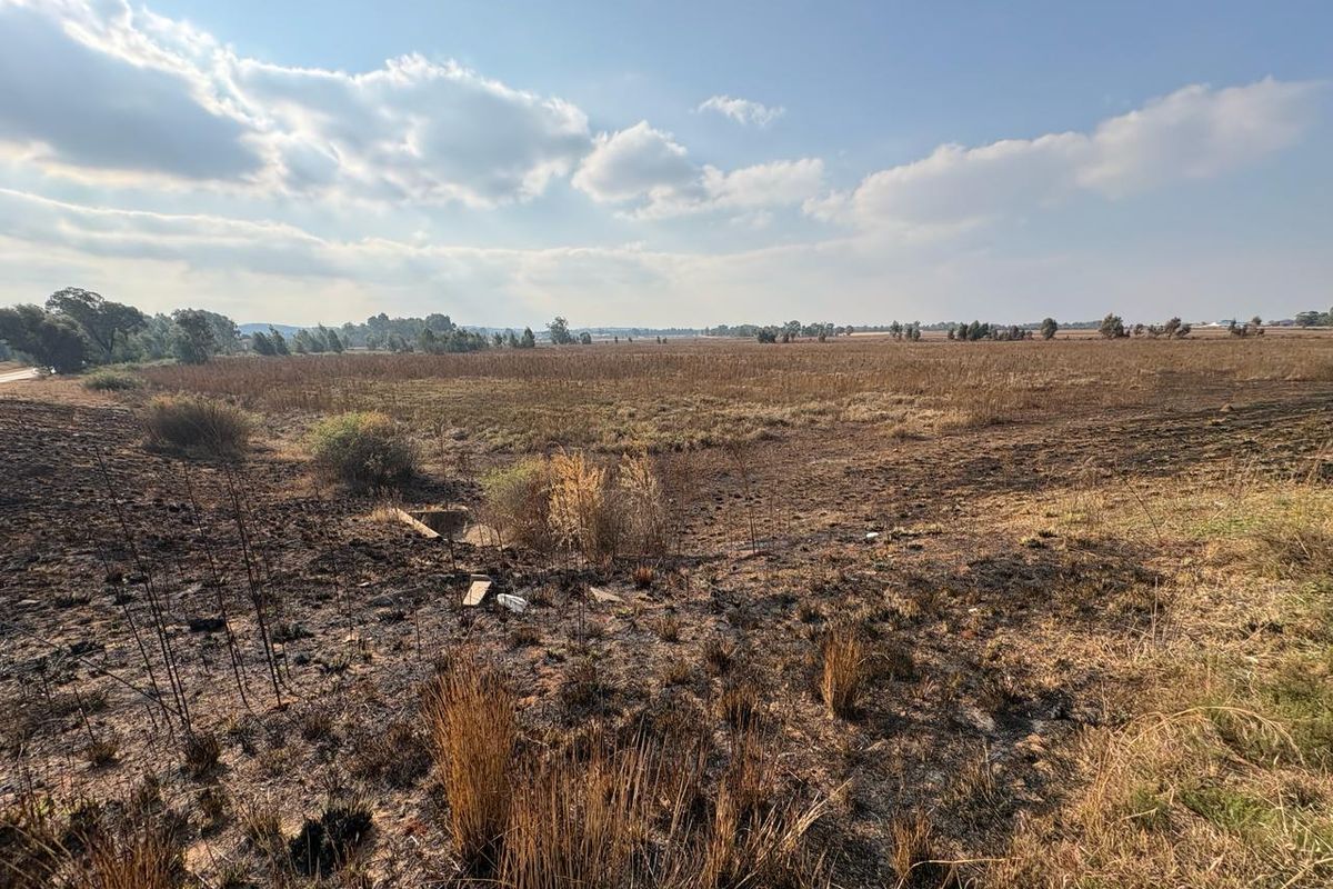 Expansive agricultural land featuring open fields with visible signs of recent fire damage to the natural vegetation.