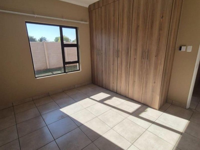 A bright, empty bedroom featuring neutral tiled flooring and floor-to-ceiling built-in wooden cupboards, offering a clean and versatile space.