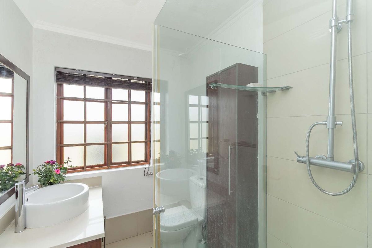 A functional bathroom featuring a glass-enclosed shower, a modern vessel sink vanity, and a window with wooden frames.