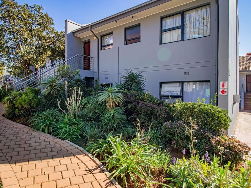 A well-maintained townhouse exterior featuring a paved walkway, landscaped garden, and modern staircase leading to the upper level entrance.