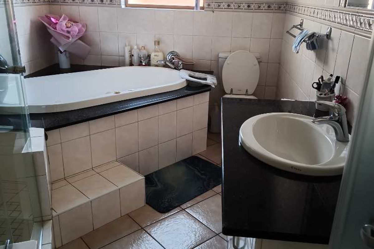 A functional bathroom featuring a built-in bathtub, a vanity with a granite countertop, and tiled finishes throughout.