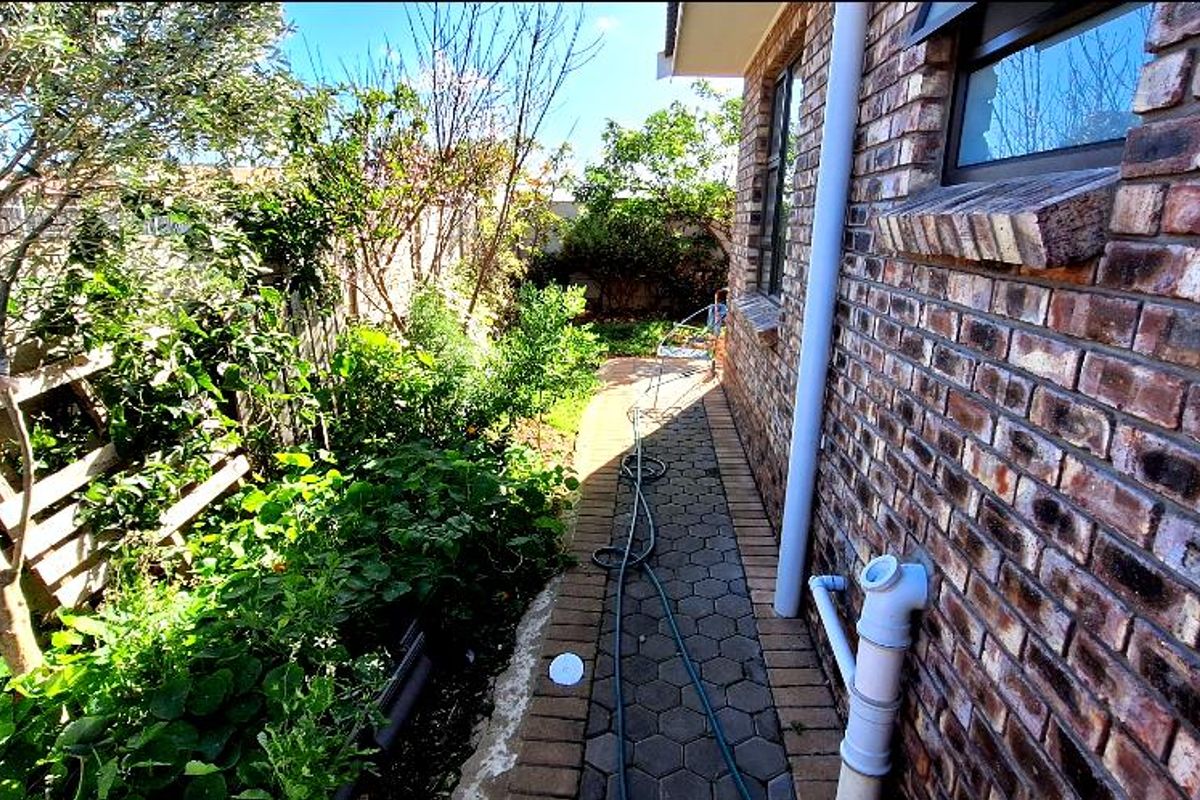 A side garden pathway featuring brick walling, paved walkway, and established garden beds along the side of the house.