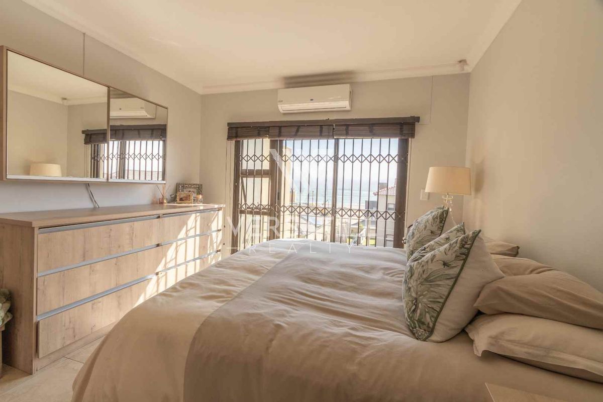 A well-maintained bedroom featuring a wall-mounted air conditioning unit, large sliding glass doors with security bars, and neutral wall finishes.