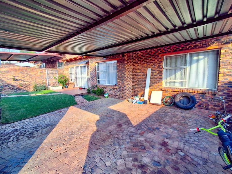 A covered outdoor patio area featuring brick walls, paved flooring, and a corrugated metal roof, providing a functional space for outdoor living.