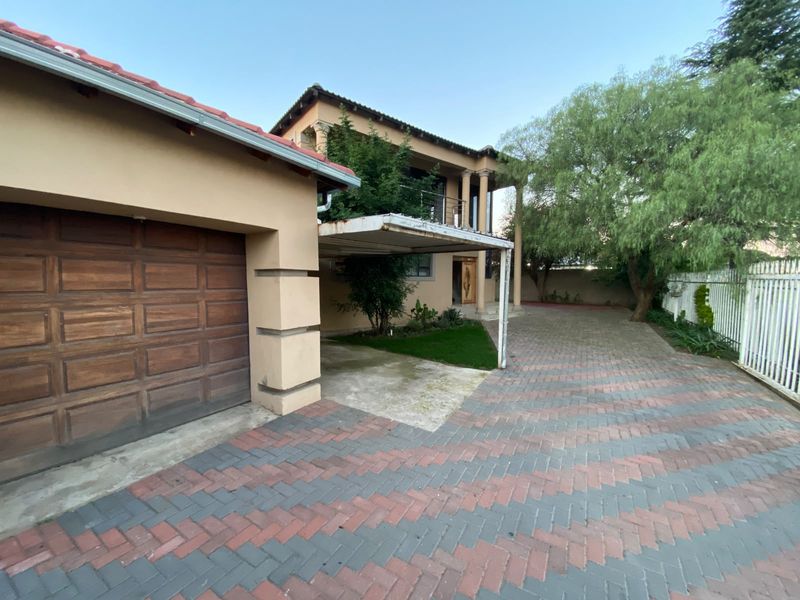 Front exterior view of the property featuring a paved driveway, attached garage, and a covered carport area with an upper-level balcony.