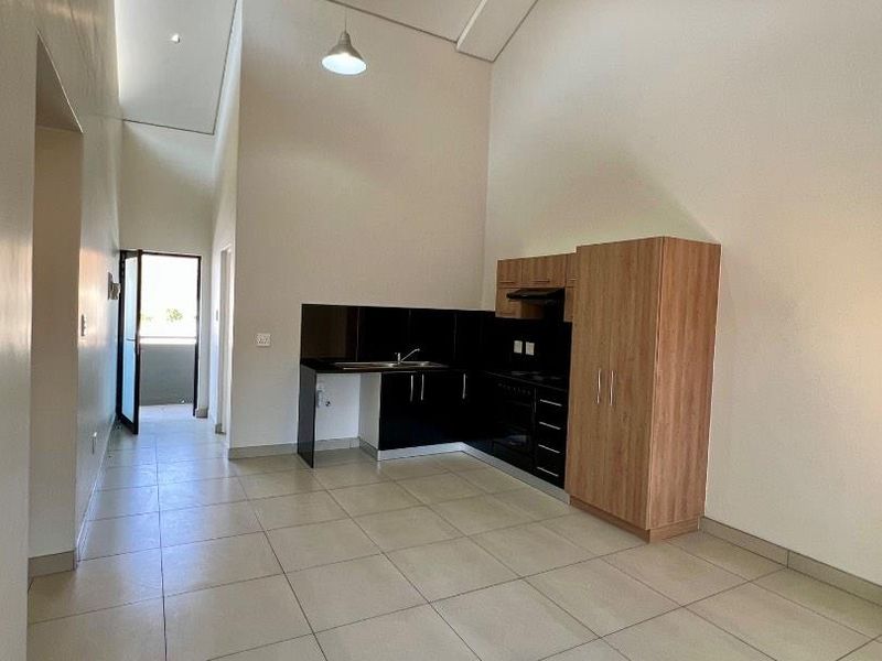 Open-plan kitchen area featuring modern cabinetry, integrated appliances, tiled flooring, and high ceilings with pendant lighting, leading to an outdoor balcony.