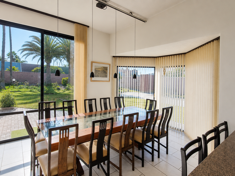 Bright dining area featuring large sliding glass doors with garden views, tile flooring, and modern pendant lighting, seamlessly connected to the kitchen space.