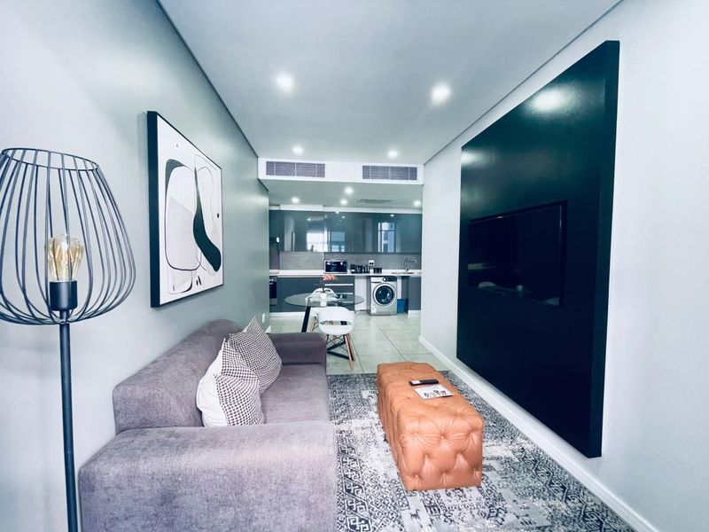 Modern open-plan living area featuring a sleek kitchen with built-in cabinetry and a dedicated wall-mounted television feature panel.