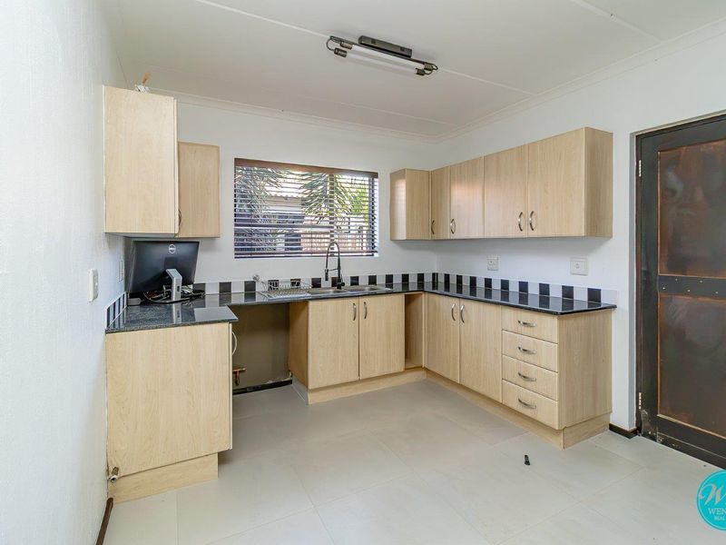 A functional kitchen featuring light wood-finish cabinetry, dark granite countertops, a tiled backsplash, and neutral floor tiles.