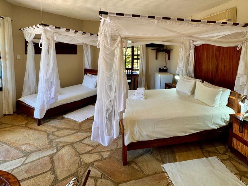 A spacious lodge bedroom featuring natural stone flooring, timber wall accents, and large windows, creating a rustic and comfortable atmosphere.