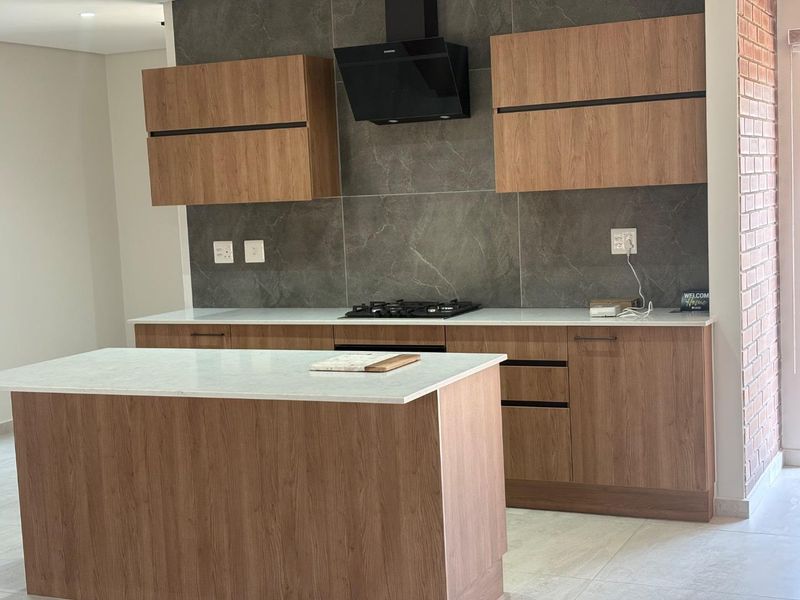 Modern kitchen featuring wood-finish cabinetry, stone countertops, a central island, and a sleek tiled backsplash with integrated gas hob and extractor fan.