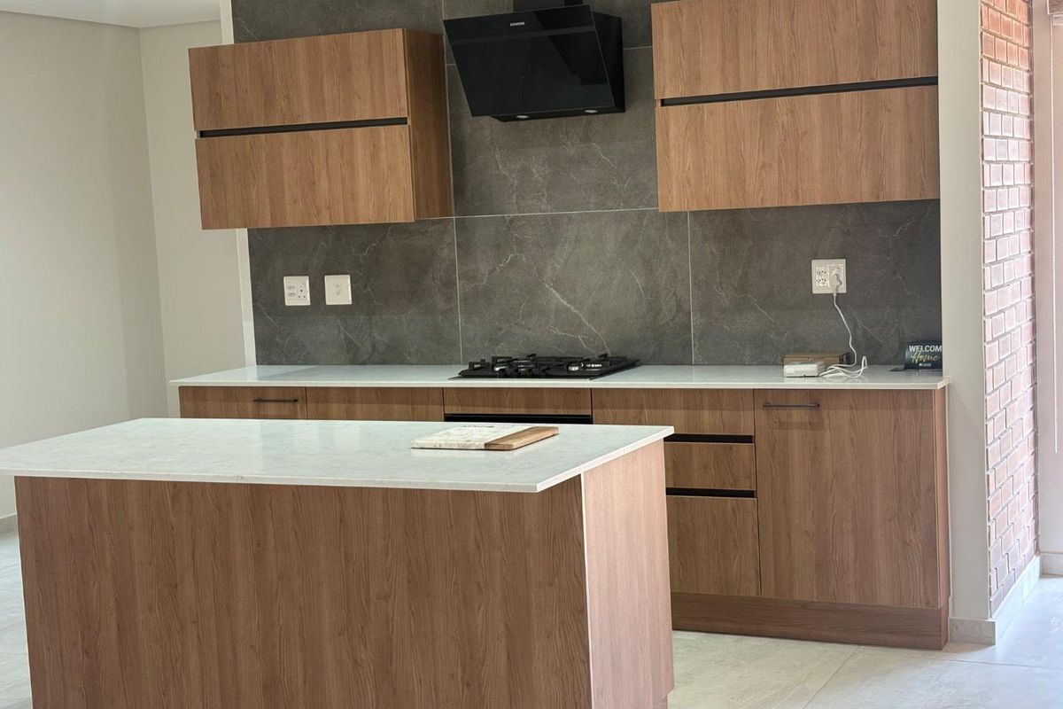 Modern kitchen featuring wood-finish cabinetry, stone countertops, a central island, and a sleek tiled backsplash with integrated gas hob and extractor fan.