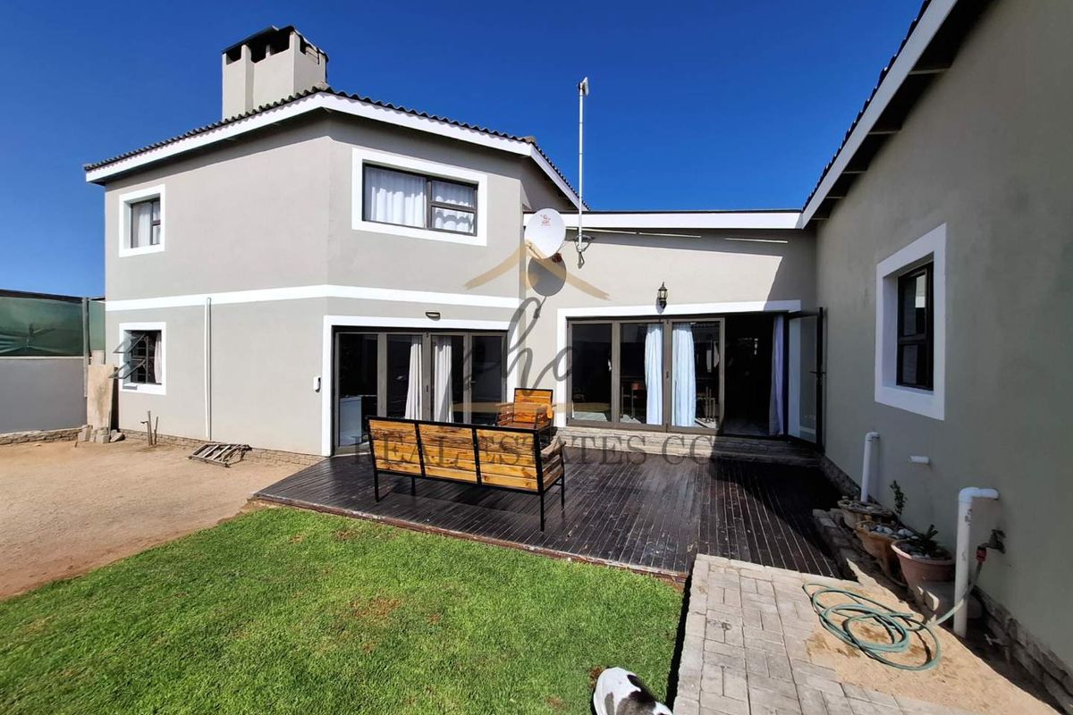 Rear view of the property featuring a timber deck, paved walkway, and access to the interior through large sliding glass doors.