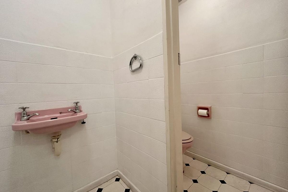 A dated bathroom featuring vintage pink sanitary ware, white wall tiling, and a classic black and white checkered floor pattern.