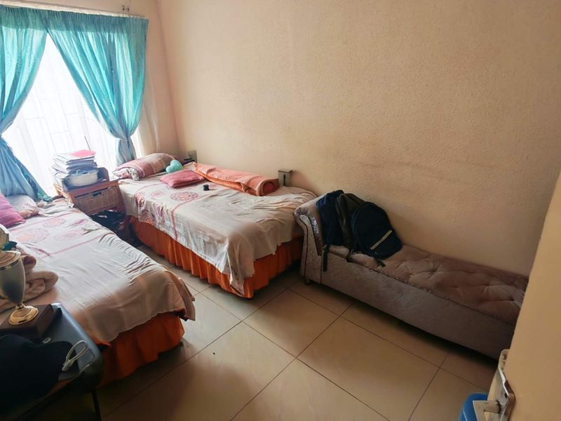 A functional bedroom featuring tiled flooring and large windows with curtain rails, offering a simple and practical living space.