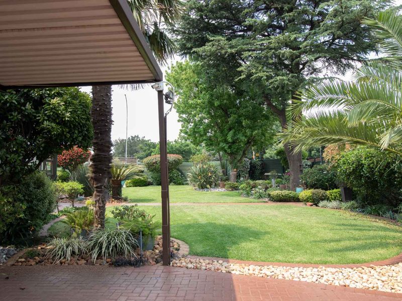 A well-maintained covered patio overlooking a lush, landscaped garden with mature trees and manicured lawn.