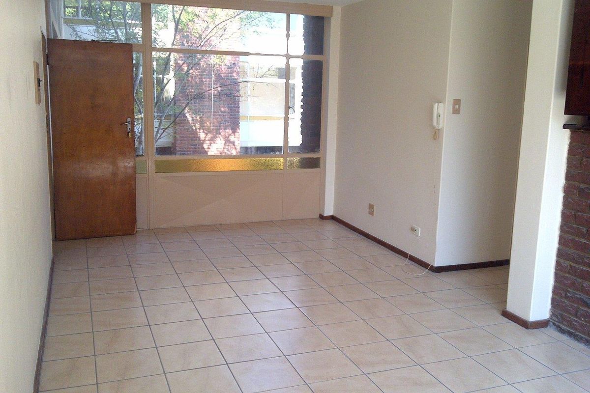 An empty living room featuring tiled flooring, a brick fireplace, and a large window panel with an integrated timber door.