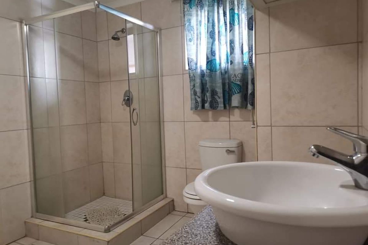 A functional bathroom featuring a glass-enclosed shower, a pedestal-style basin, and tiled walls and flooring.