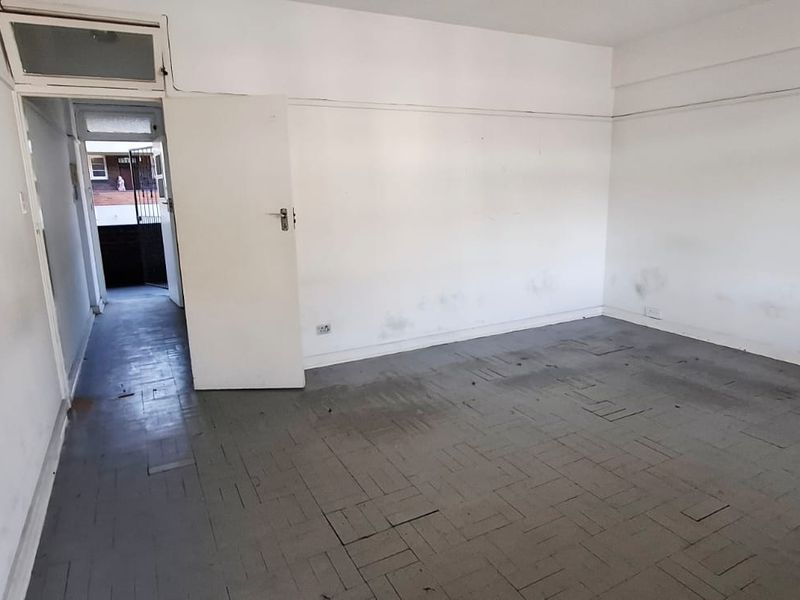 An empty bedroom featuring parquet flooring and a transom window, requiring cosmetic updates to the walls and flooring to restore its condition.