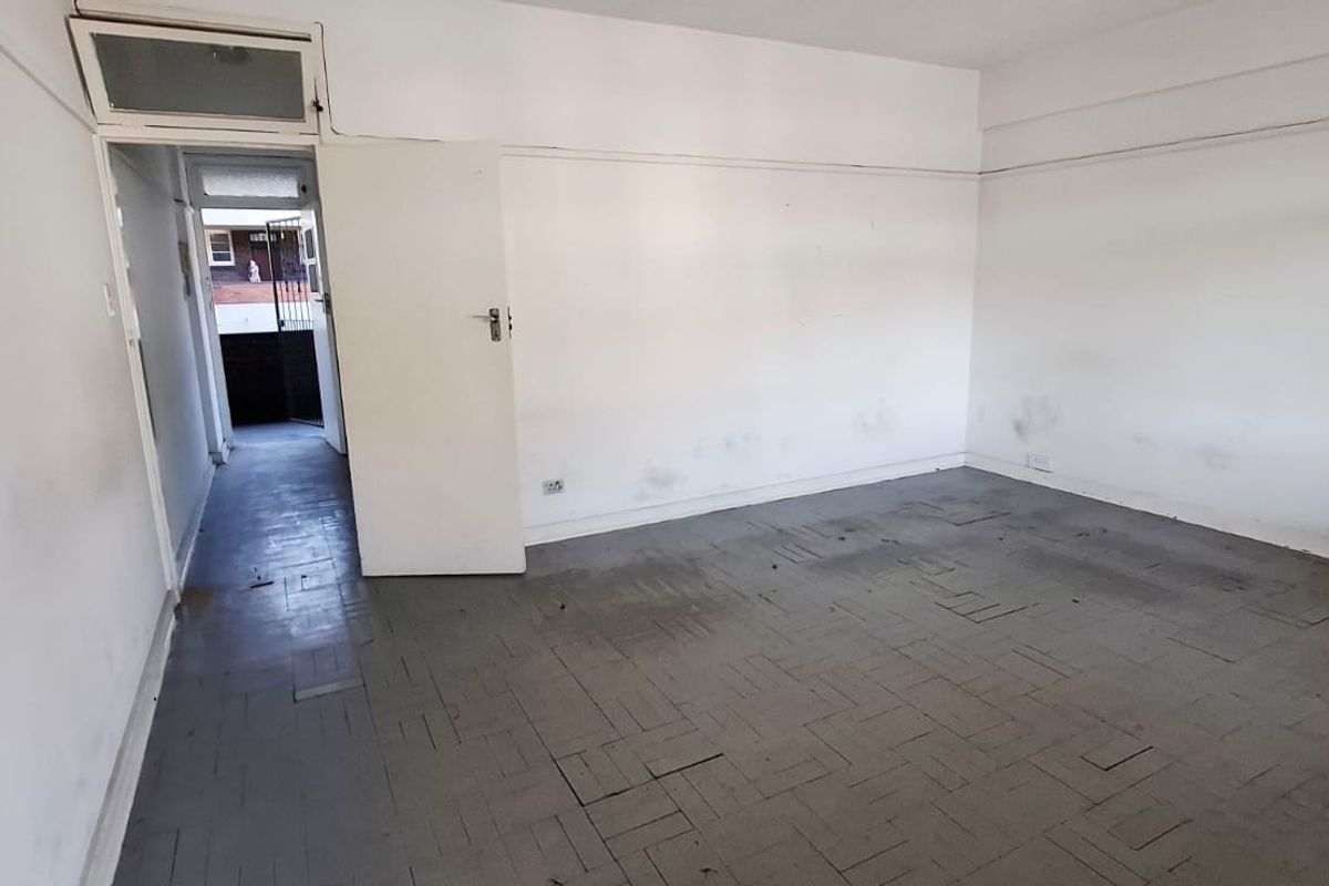 An empty bedroom featuring parquet flooring and a transom window, requiring cosmetic updates to the walls and flooring to restore its condition.