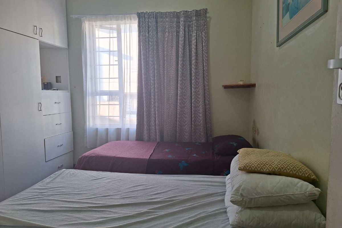 A bedroom featuring built-in cabinetry and a window with curtains, showing signs of wear on the walls.