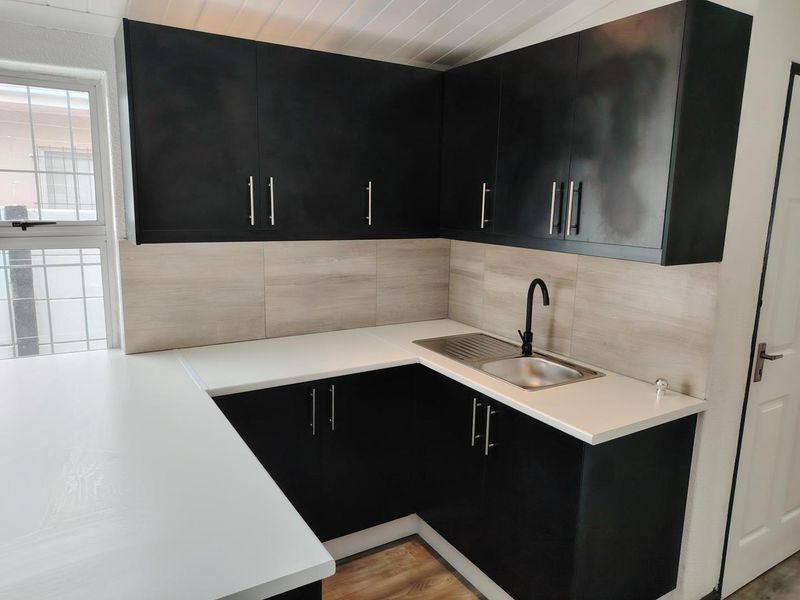 Modern kitchen featuring sleek black cabinetry, white countertops, a stainless steel sink with a black mixer tap, and wood-look tile backsplash.