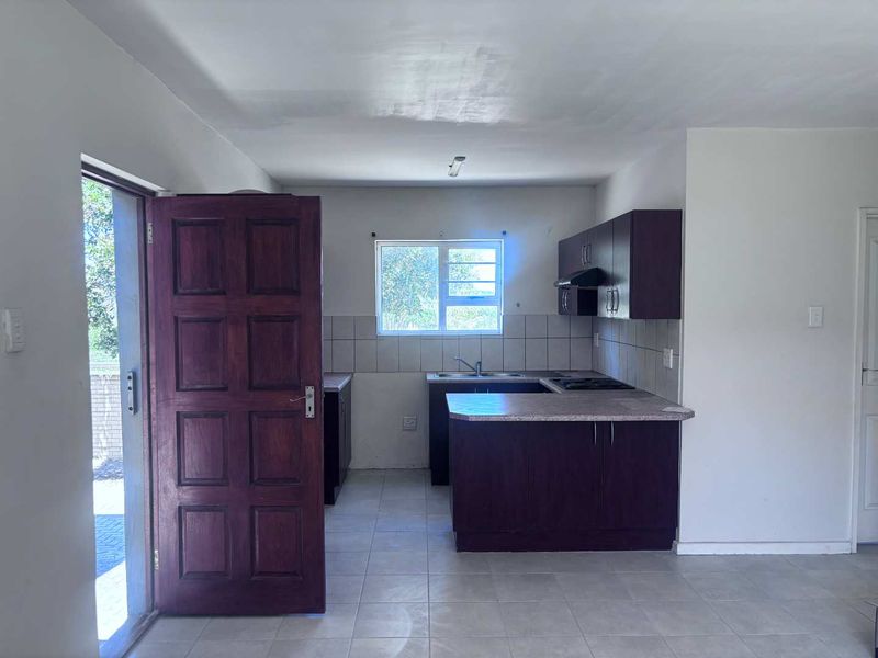 A functional kitchen featuring dark cabinetry, laminate countertops, a built-in hob with extractor fan, and tiled flooring in an open-plan layout.