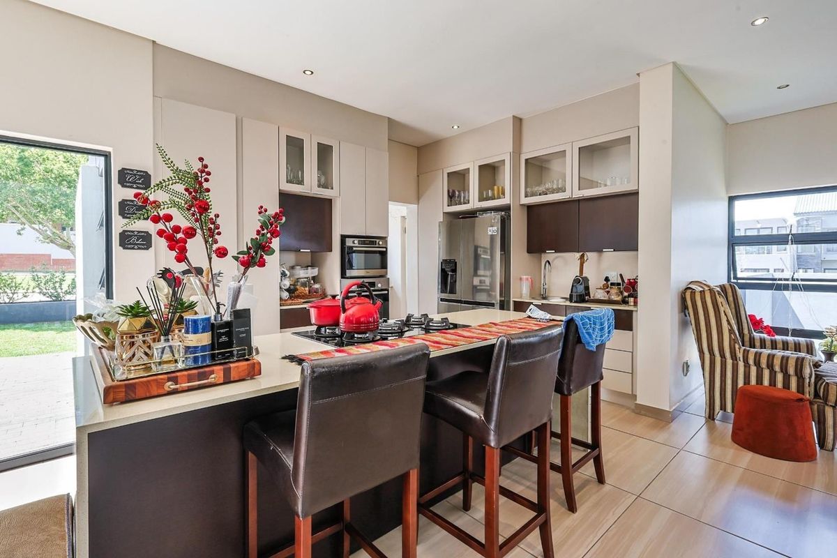 Modern open-plan kitchen featuring a central island with a gas hob, built-in oven, and sleek cabinetry, seamlessly connecting to the outdoor patio area.