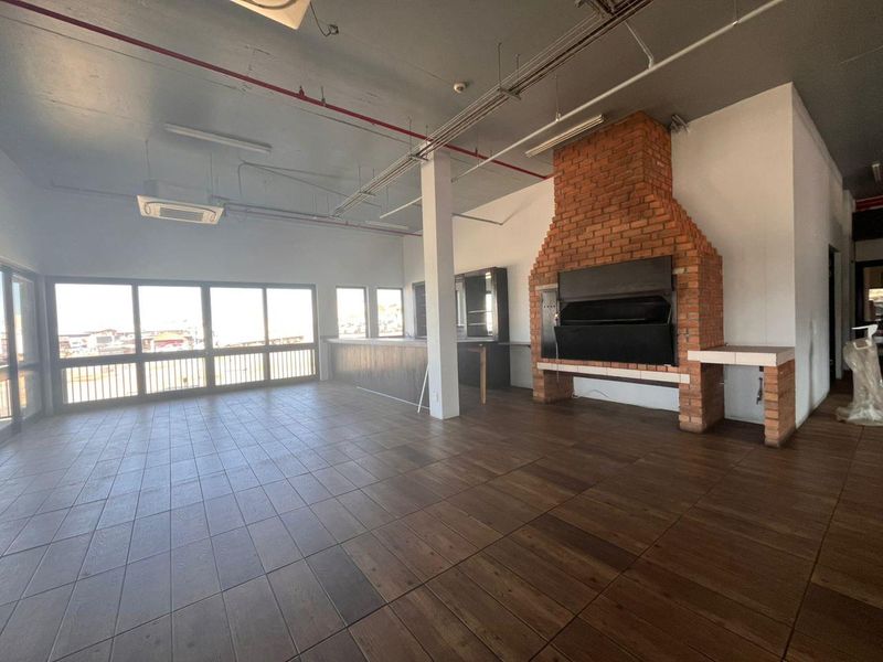 Spacious open-plan industrial area featuring a prominent built-in brick fireplace, bar counter, tiled flooring, and large windows with ample natural light.