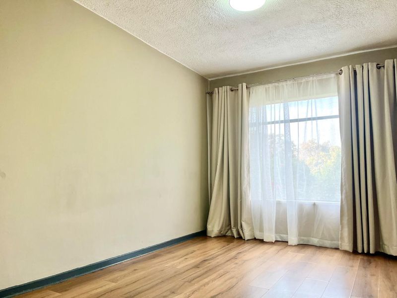 A bright, empty bedroom featuring laminate flooring, neutral wall tones, and a large window with curtain tracks, offering a blank canvas for personalization.