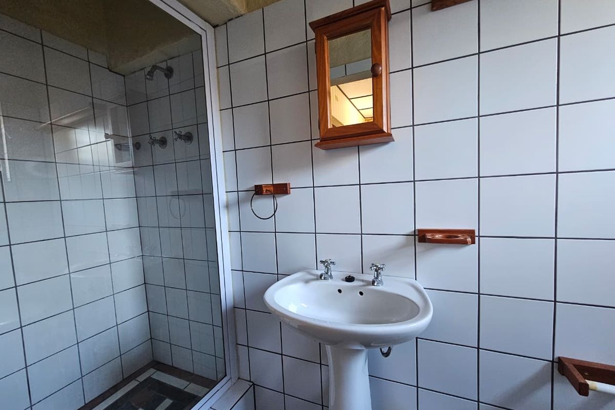 A functional bathroom featuring a pedestal basin, a glass-enclosed shower, and white wall tiling with dark grout.