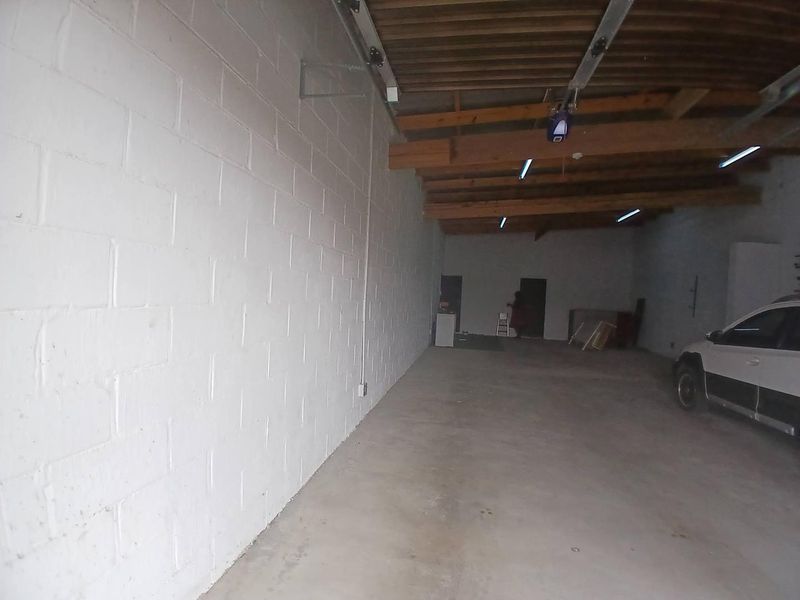 Spacious garage featuring exposed timber ceiling beams, painted brick walls, and a concrete floor, offering ample storage or parking space.