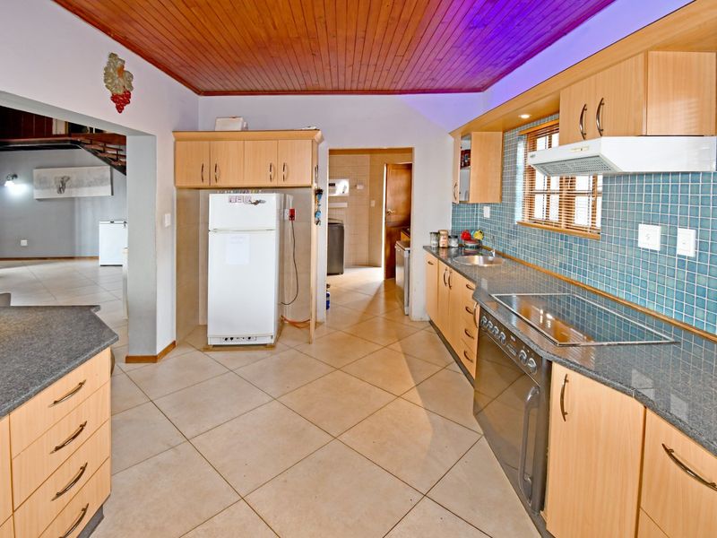 Functional kitchen featuring light wood cabinetry, granite countertops, tiled backsplash, and a timber ceiling, with an adjacent scullery area.