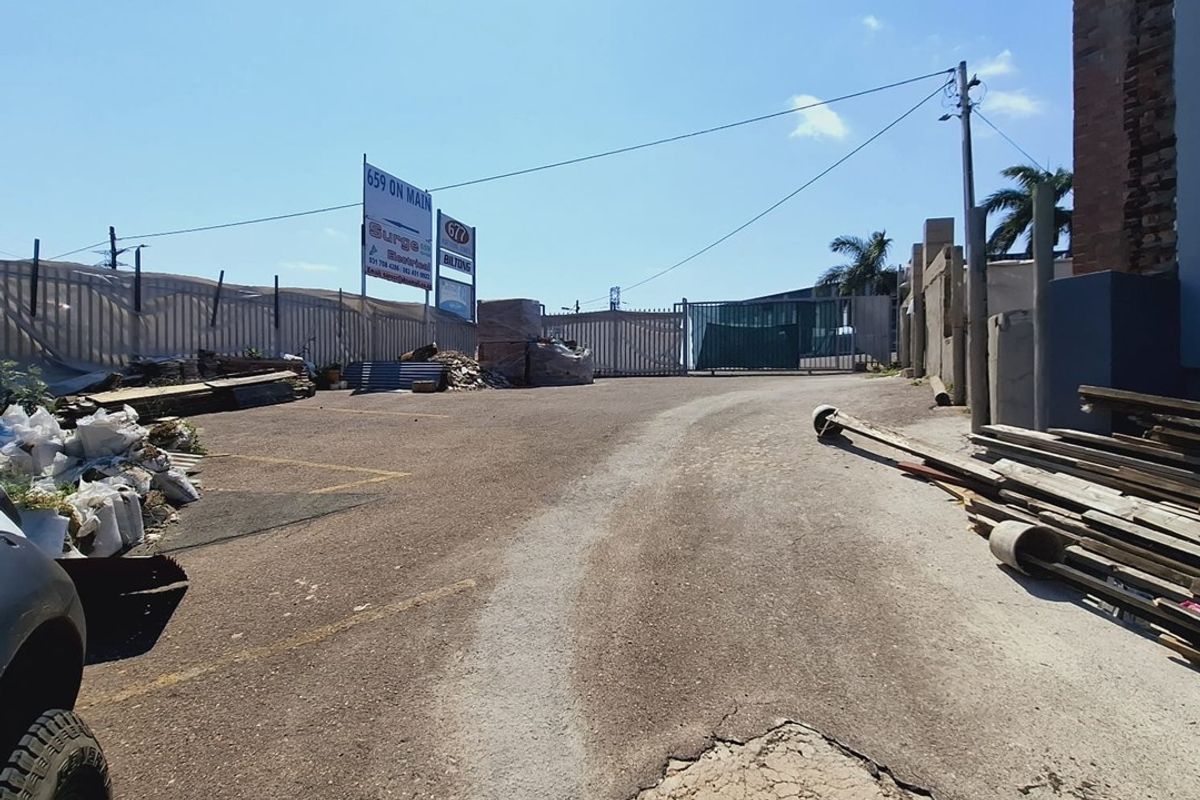Rear exterior area featuring asphalt paving, perimeter fencing, and a security gate, showing significant surface wear and maintenance requirements.