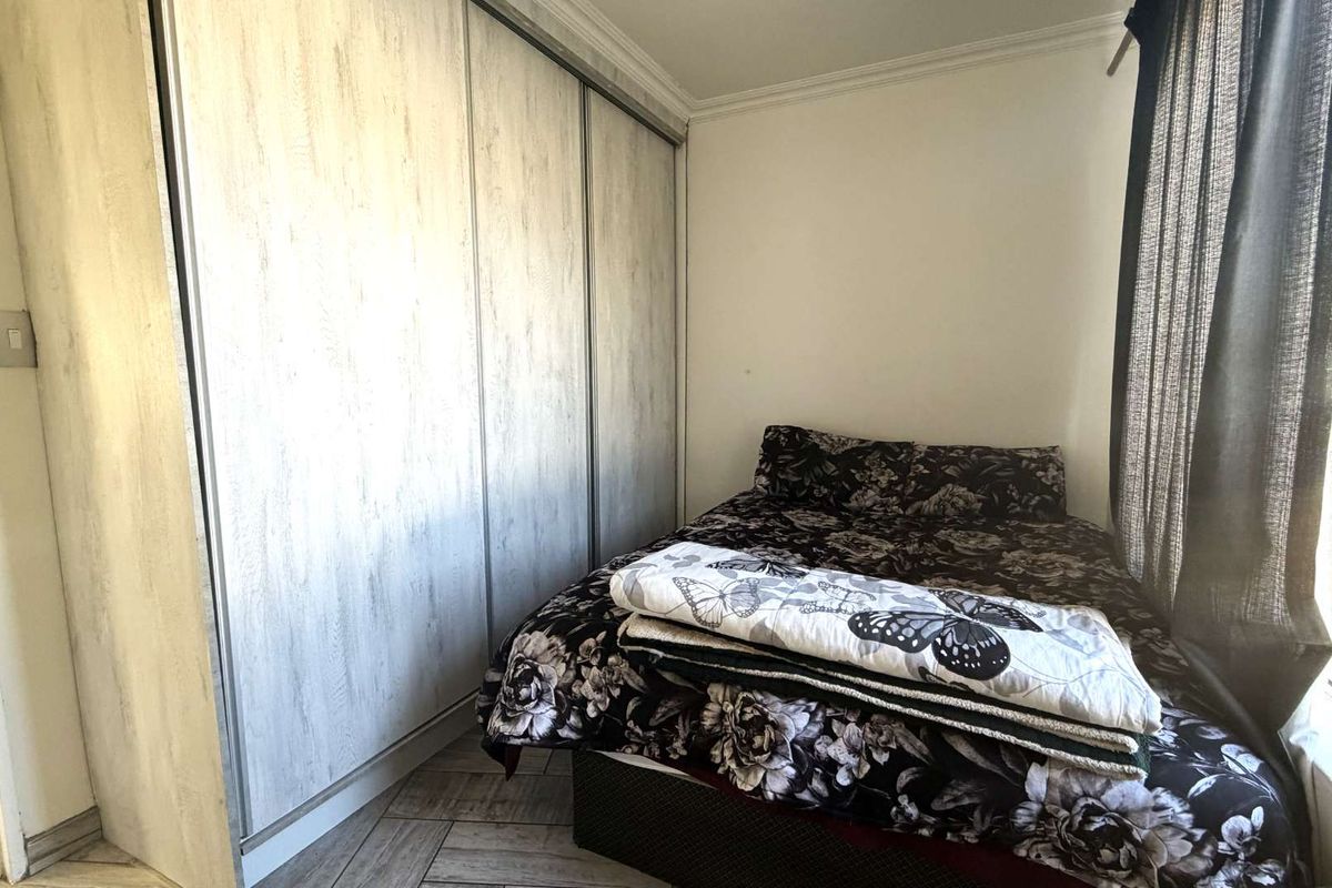 A bedroom featuring built-in sliding door cupboards with a wood-grain finish and tiled flooring.
