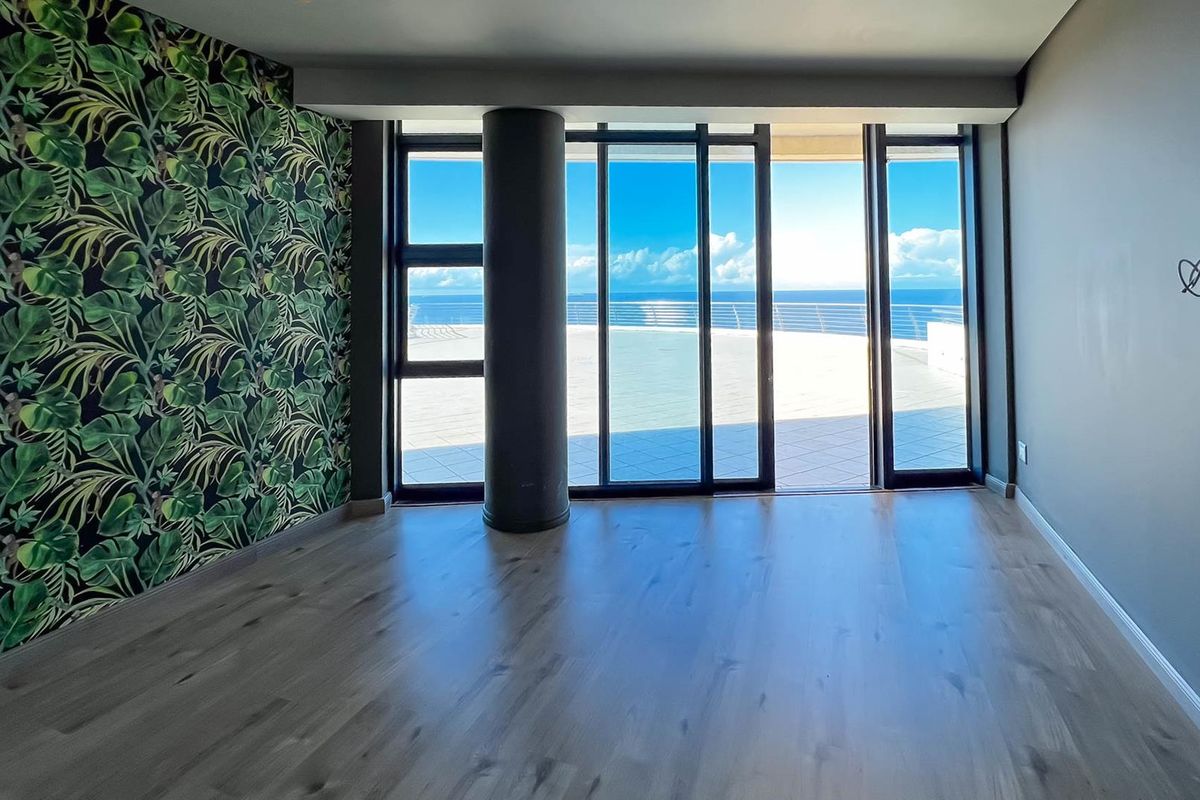 Spacious living area featuring wood-look flooring, a bold feature wall, and large sliding glass doors opening onto a balcony with ocean views.