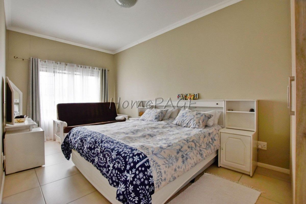 A well-lit bedroom featuring neutral wall tones, tiled flooring, and a built-in headboard unit with integrated shelving.