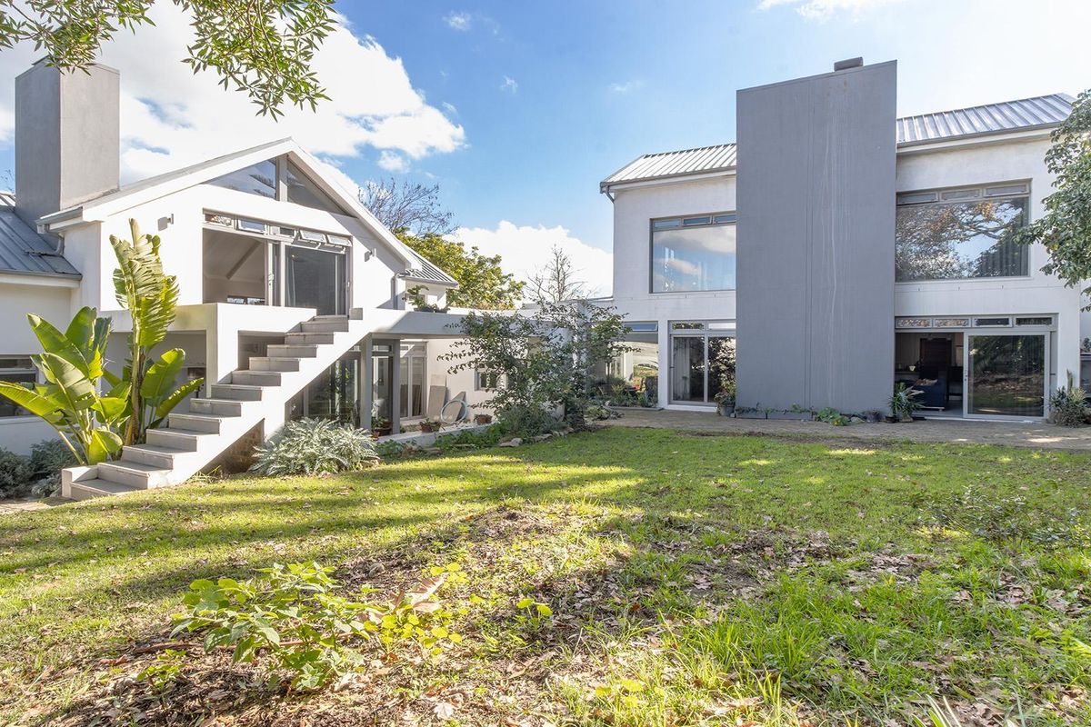 Rear view of a modern multi-level house featuring a large lawn, paved patio, external staircase, and prominent chimney stacks.