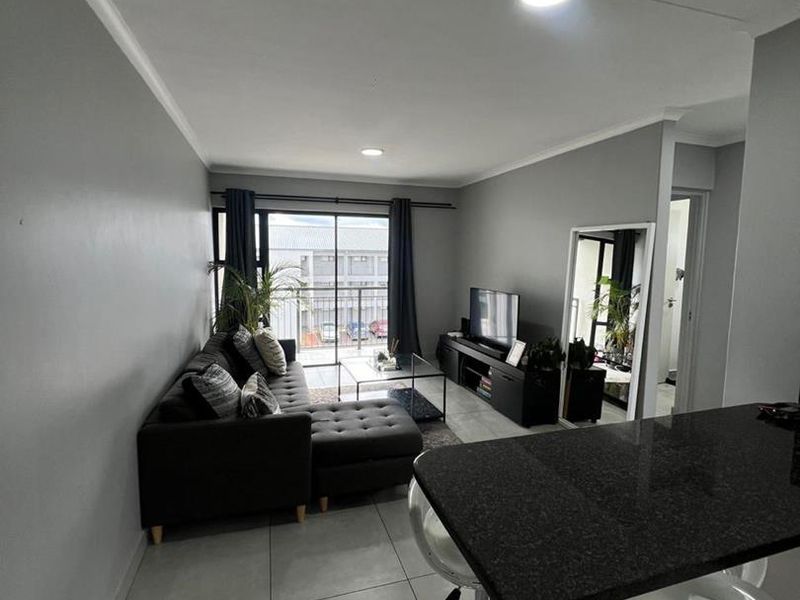 Open-plan living area featuring tiled flooring, a granite breakfast counter, and a sliding glass door leading to a balcony.