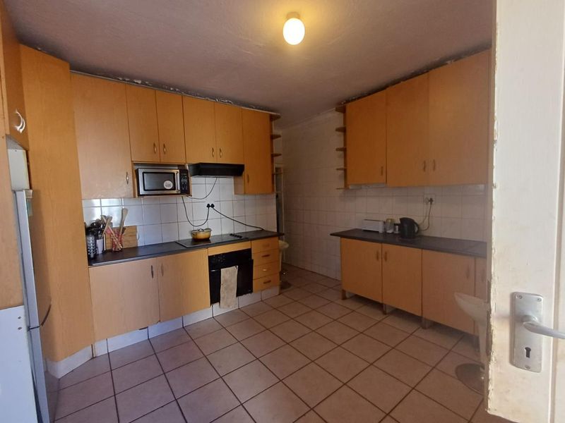 A functional kitchen featuring laminate cabinetry, built-in oven, electric hob, and tiled flooring, offering a practical layout with potential for modern updates.