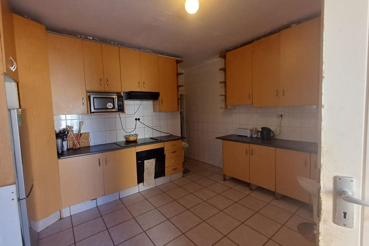 A functional kitchen featuring laminate cabinetry, built-in oven, electric hob, and tiled flooring, offering a practical layout with potential for modern updates.
