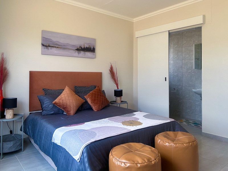 A well-maintained bedroom featuring tiled flooring, neutral walls, and direct access to an en-suite bathroom through a sliding door.