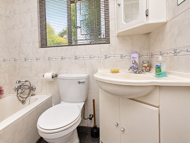 A functional bathroom featuring a bathtub, toilet, and vanity cabinet with tiled walls and a window with blinds.
