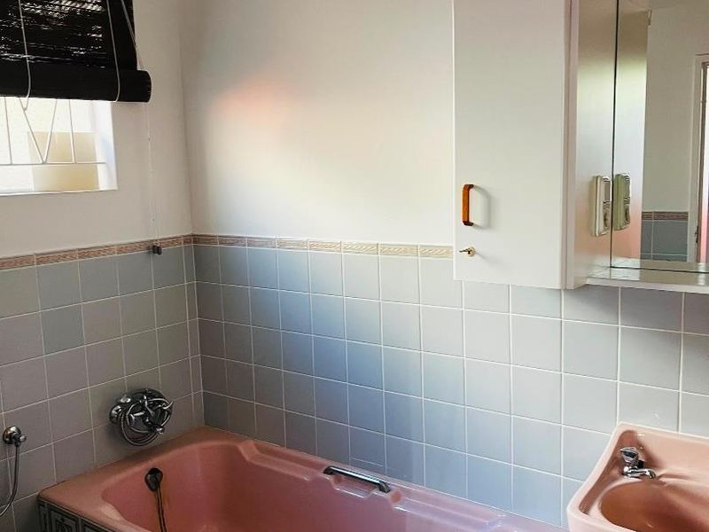 A dated bathroom featuring a pink bathtub and matching basin, complemented by light blue wall tiles and a built-in medicine cabinet.
