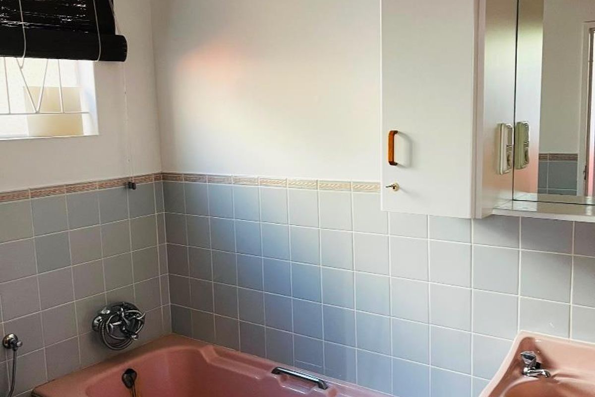 A dated bathroom featuring a pink bathtub and matching basin, complemented by light blue wall tiles and a built-in medicine cabinet.