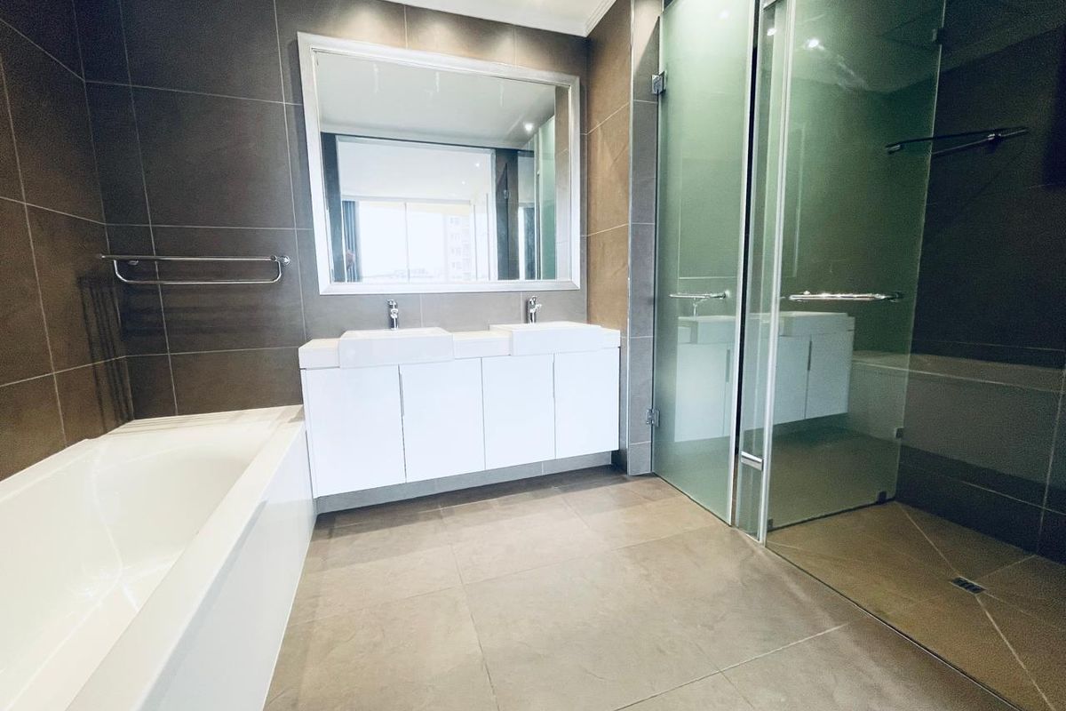 Modern bathroom featuring a double vanity, built-in bathtub, and a separate glass-enclosed shower with neutral floor-to-ceiling tiling.