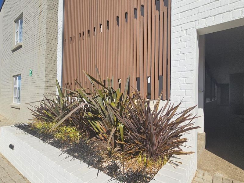 Exterior view of the apartment building entrance featuring a modern vertical timber slat screen, white brick facade, and a raised landscaped planter box.