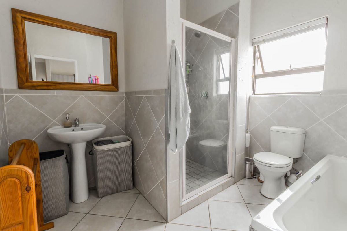 A functional bathroom featuring a pedestal basin, separate shower enclosure, toilet, and bathtub with neutral wall and floor tiling.